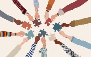 Group of multicultural business people with arms and hands in a circle holding a piece of jigsaw. Co-workers of diverse ethnic groups and cultures. Cooperate - collaborate. Teamwork