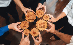 This image captures diverse hands holding interlocking wooden gears, symbolizing teamwork and collaboration essential for success in modern business settings. Amity