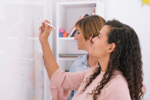 Group of creative women doing a brain storm on a whiteboard. Creative people working on new design ideas to develop startup enterprise. Entrepreneur teaching success techniques. Co working lifestyle. Group of creative women doing a brain storm on a whiteboard. Creative people working on new design ideas to develop startup enterprise. Entrepreneur teaching success techniques. Co working lifestyle.