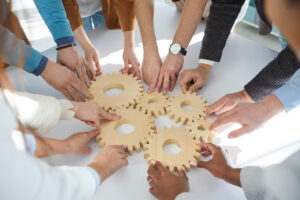 Close up of wooden gears that business people connect together during teambuilding session. Close up of wooden gears that business people connect together during teambuilding session. Male and female colleagues together find business solutions and contribute to development of business.